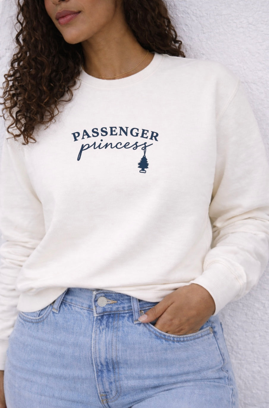 Person wearing a white sweatshirt with 'Passenger Princess' text and graphic, standing against a neutral background.