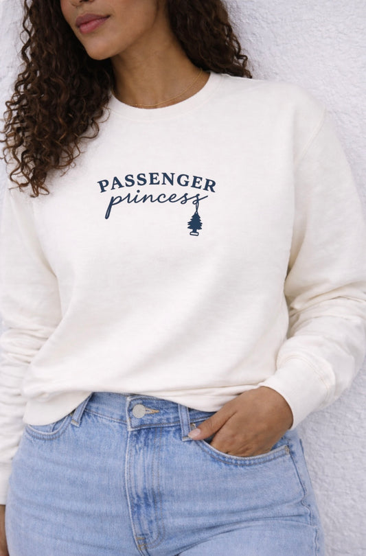 Person wearing a white sweatshirt with 'Passenger Princess' text and graphic, standing against a neutral background.
