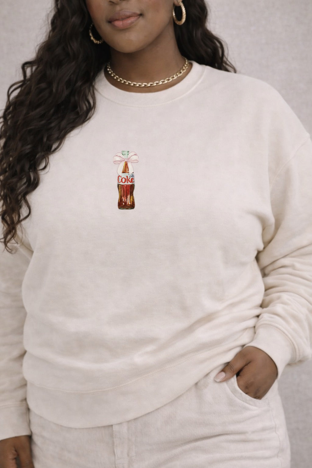 Person wearing a ivory sweatshirt with a soda graphic design on a gray background