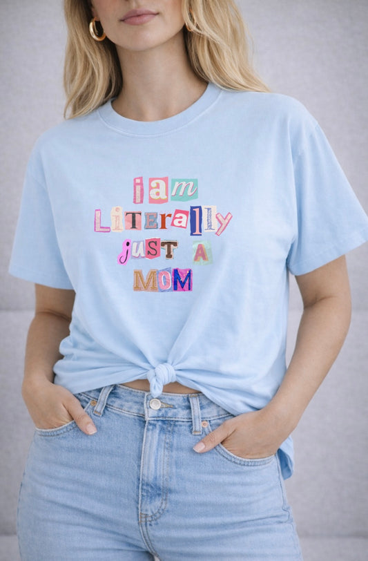 Person wearing a light blue t-shirt with colorful text design "I am Literally Just a Mom" and light blue jeans.