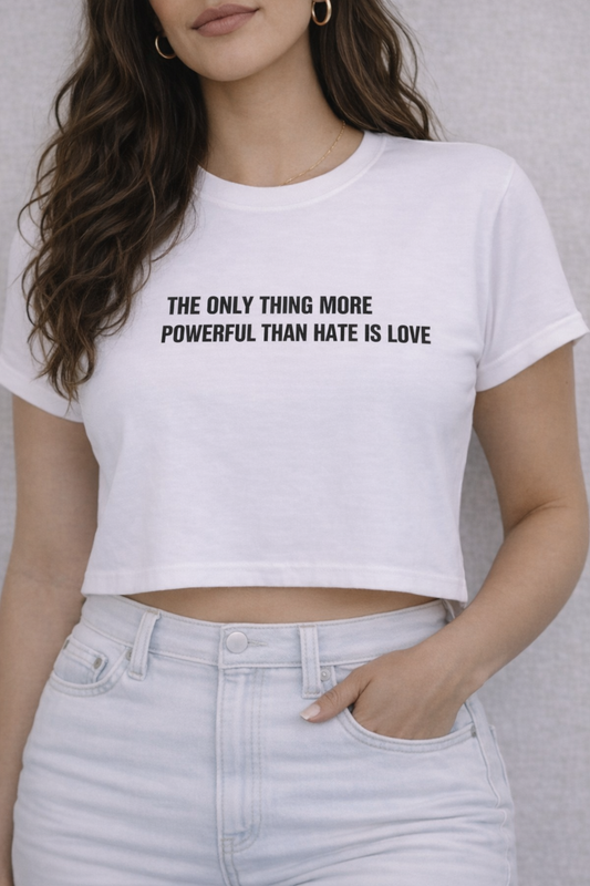 Person wearing a white crop top with a motivational quote "THE ONLY THING MORE POWERFUL THAN HATE IS LOVE" on a plain background