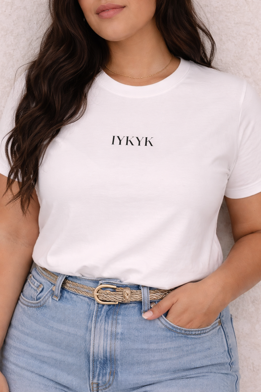 Person wearing a white t-shirt with 'IYKYK' text and blue jeans.