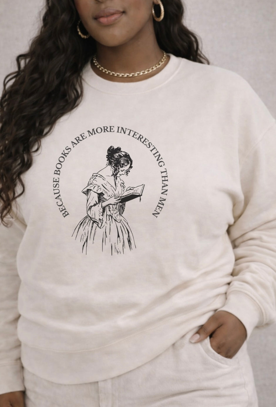 Person wearing a white sweatshirt with a graphic design and text. reading "Because Books are more interesting than men"
