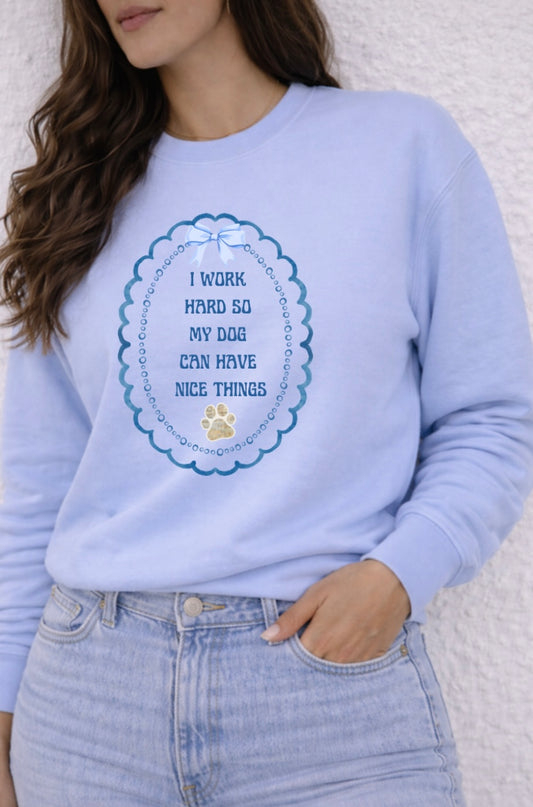 Light blue sweatshirt with text that says "I work hard so my dog can have nice things" and paw print design worn by a person against a white background
