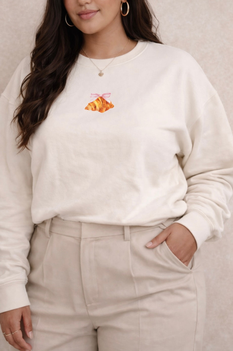 Person wearing a ivory sweatshirt with a small croissant design on a neutral background