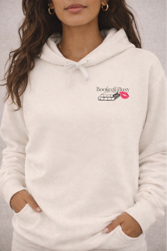 White hoodie with a brand logo that says "Booked & Busy"  worn by a person against a neutral background