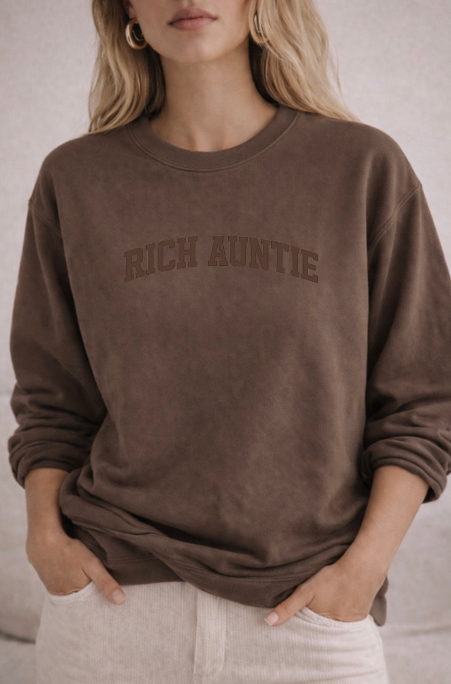 Person wearing a brown sweatshirt with 'RICH AUNTIE' text on a neutral background
