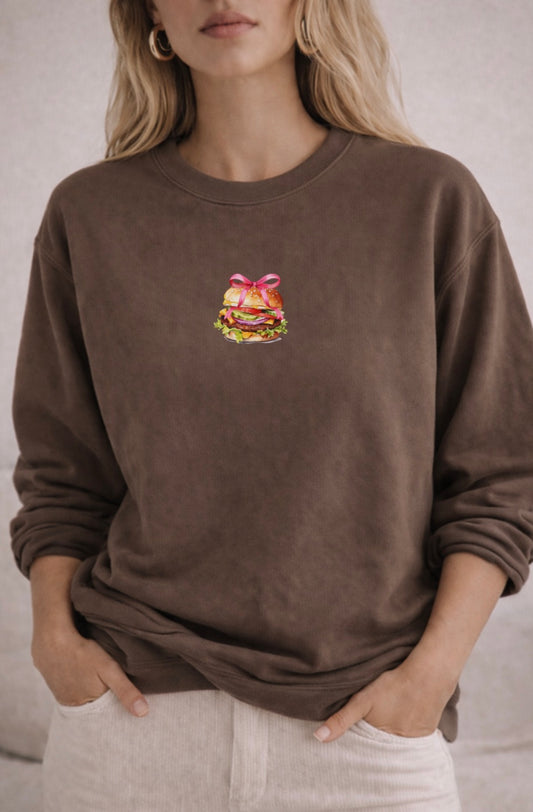 Brown sweatshirt with a colorful cheeseburger graphic on a neutral background