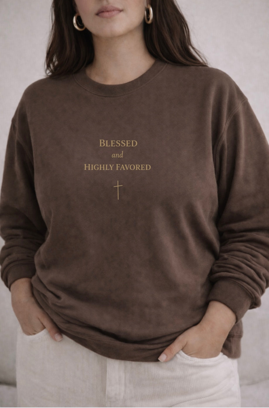 Person wearing a brown sweatshirt with 'Blessed and Highly Favorable' text and cross symbol.