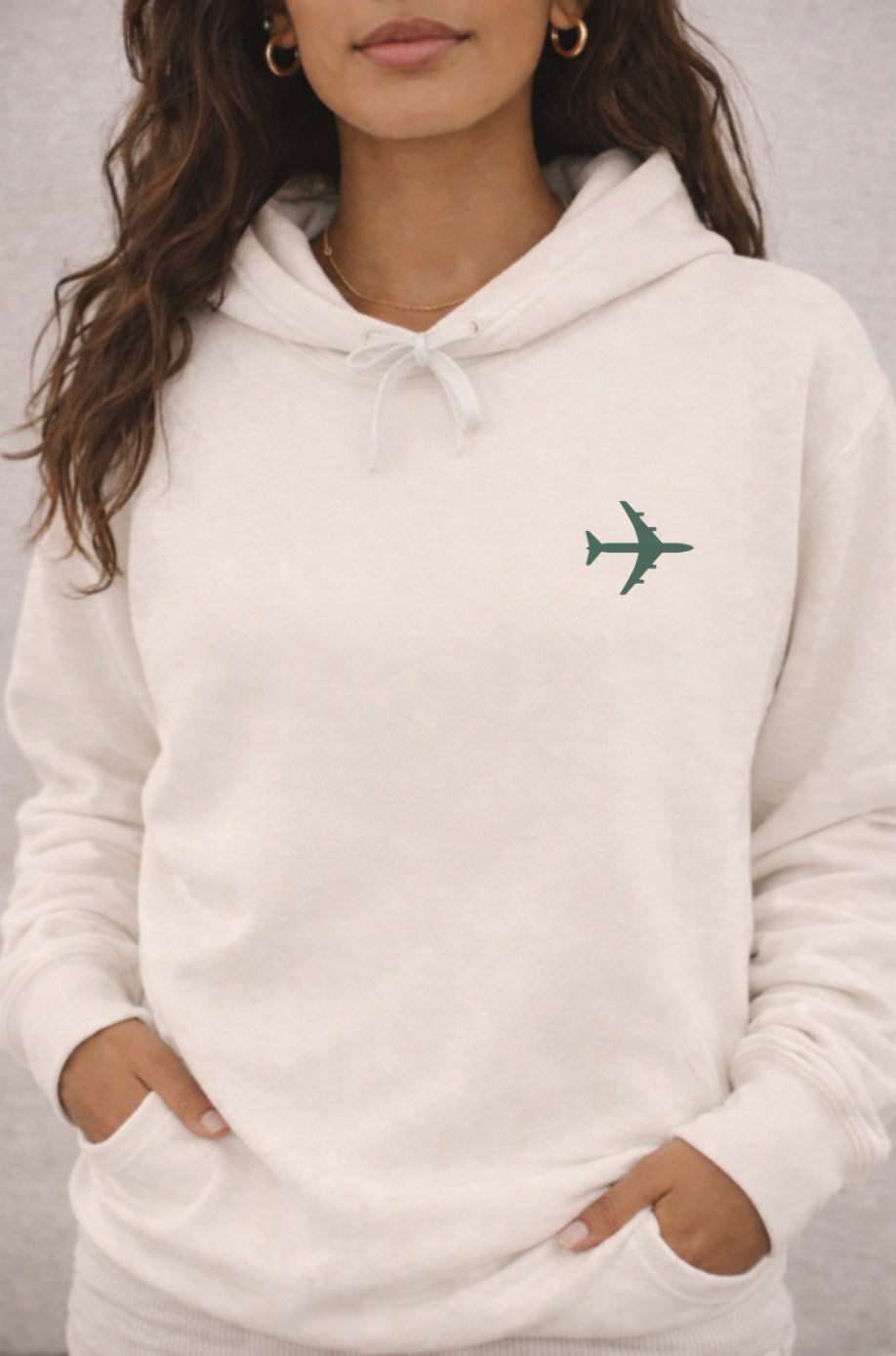 ivory hoodie with a green airplane emblem worn by a person on a gray background